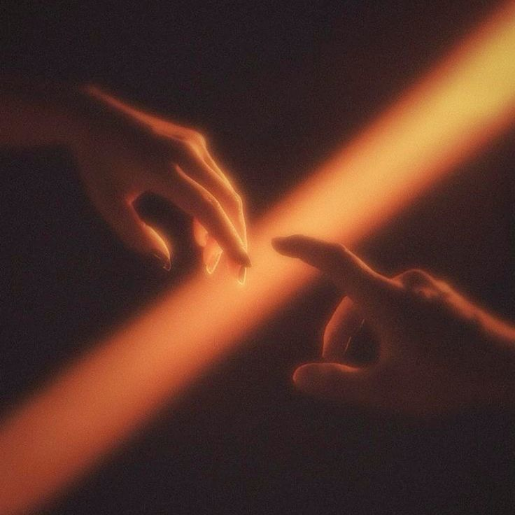 Two hands reaching toward each other through a warm beam of light, their fingertips almost touching.